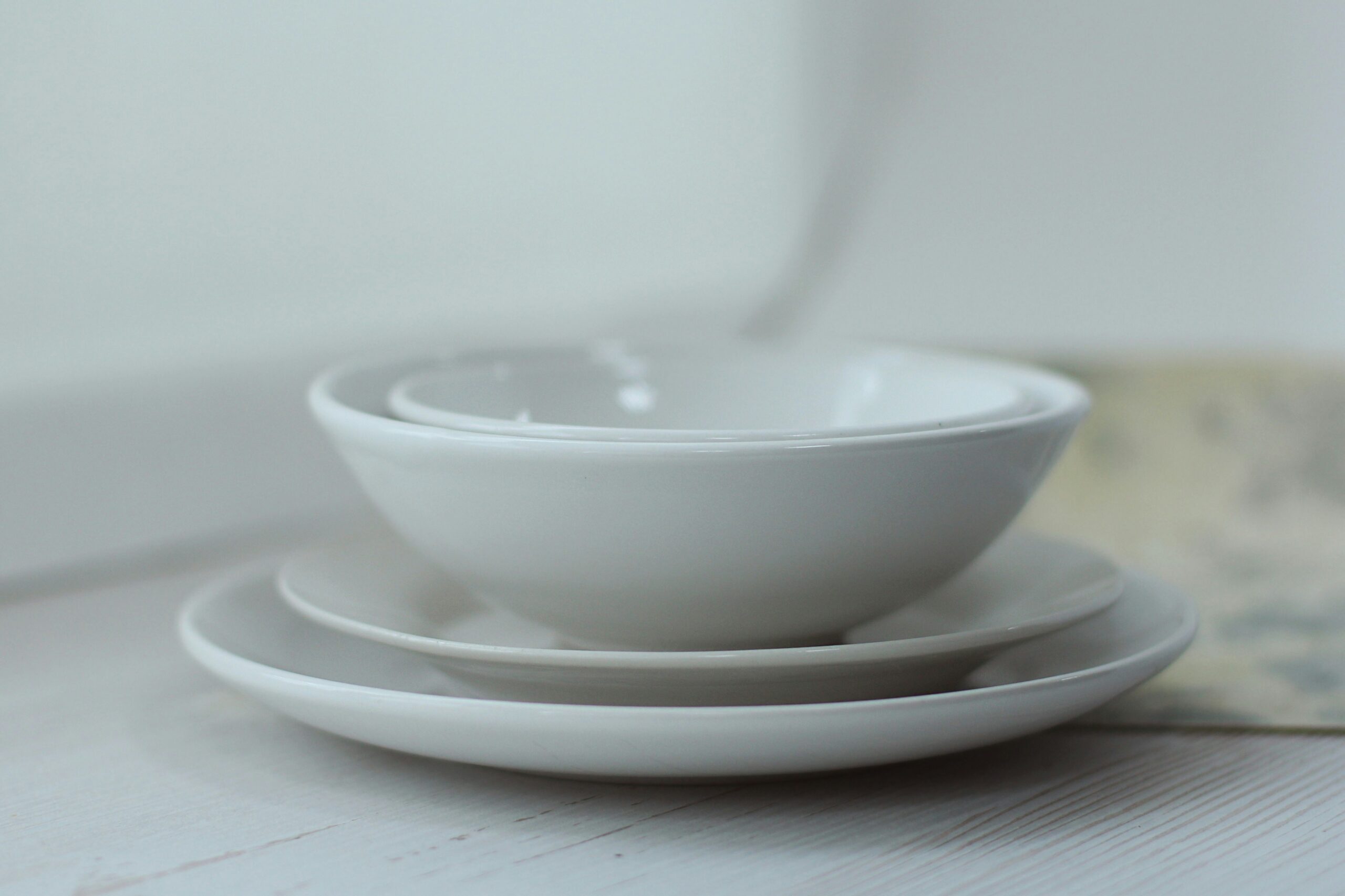 Stack of white ceramic bowls and plates on a wooden surface, with a soft background.